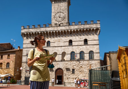 Montepulciano, Tuscany, Italy. August 2020. In the town hall square a Caucasian woman with a tourist map looks around, selective focus on the woman. Behind her the town hall.のeditorial素材