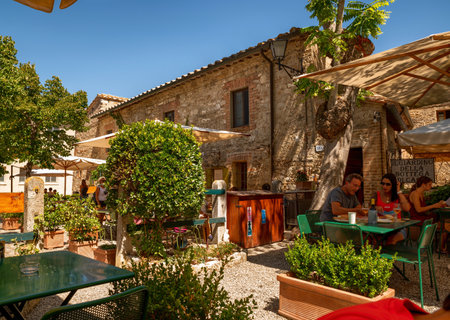 Bagno Vignoni, Tuscany, Italy. August 2021. In the center of the village a restaurant with outdoor tables and umbrellas in a very charming setting.のeditorial素材