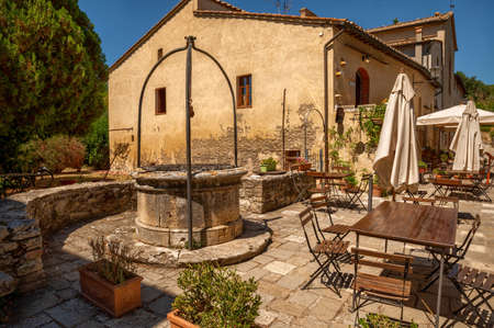 Bagno Vignoni, Tuscany, Italy. August 2020. In the center of the village a restaurant with outdoor tables and umbrellas, an ancient well gives the context a lot of charm.のeditorial素材