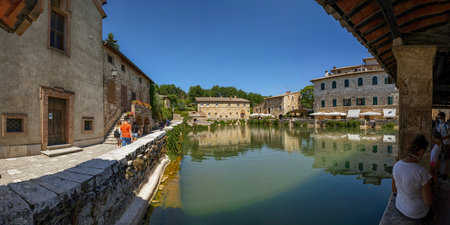 Bagno Vignoni, Tuscany, Italy. August 2020. A large natural outdoor thermal hot water pool is point of interest for tourists. Large panoramic format photo.のeditorial素材