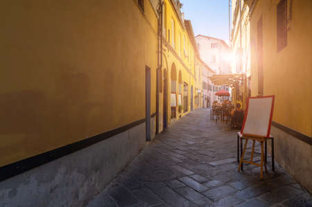 Lucca, Tuscany, Italy. August 2020. In an alley in the historic center, the tables of a restaurant with seated customers. Street paved with stones, the colorful facades of the houses frame it.の写真素材