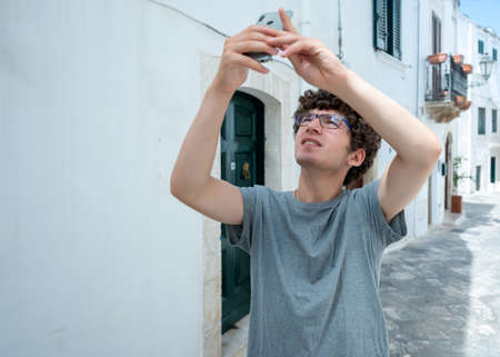 Ostuni, Puglia, Italy. August 2021. A young Caucasian is busy taking pictures of him with his mobile...