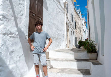 Ostuni, Puglia, Italy. August 2021. A young Caucasian is posing for a souvenir photo in one of the white alleys of the historic center of the village. Concept of young people on vacation.の写真素材