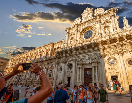 Lecce, Puglia, Italy. August 2021. The church of Santa Croce is the finest example of Lecce baroque. A tourist is photographing her with her mobile phone. People in front of the entrance.のeditorial素材