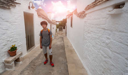 Alberobello, Puglia, Italy. August 2021. A young man with curly hair and glasses observes the characteristic environment of the village, behind him the characteristic houses..の写真素材