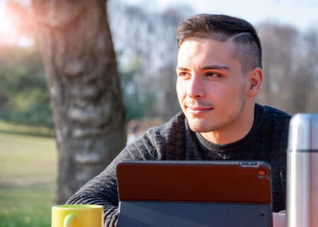 Portrait of smiling young man works remotely in a park on a beautiful sunny day.  Remote work...