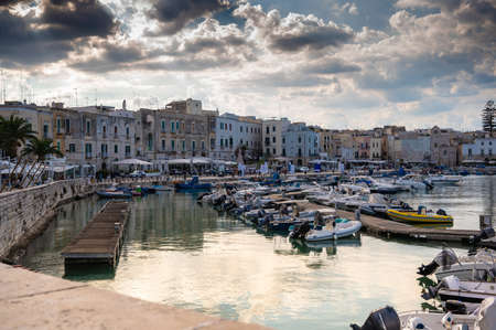 Trani, Puglia, Italy. August 2021. Beautiful view of the marina surrounded by houses with colored facades, dramatic sky with rays of light filtering through the clouds.のeditorial素材