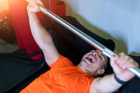 Amazing image of a young man doing bench press with a maximum weight. He screams in the effort. Exciting and motivational photo.の写真素材