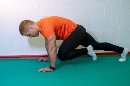 Young muscular male athlete trains mountain climbing ground exercise. Background with blank wall, copy space.の写真素材