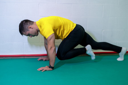 Young muscular male athlete trains mountain climbing ground exercise. Background with blank wall, copy space.の写真素材
