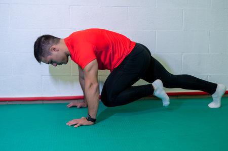 Young muscular male athlete trains mountain climbing ground exercise. Background with blank wall, copy space.の写真素材