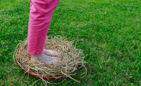 Shot with a close-up on the feet of a barefoot Caucasian woman, she is taking a sensorial journey in nature: she is inside a basket lined with straw. Nice sunny day.の写真素材