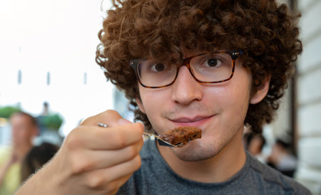 Vienna, Austria, August 18, 2022. Portrait of a friendly young Caucasian man smiling and looking at the camera while about to eat a piece of chocolate cake, a specialty of Austrian pastry. Positivity.の写真素材