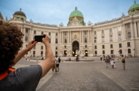 Vienna,Austria,August 18, 2022. In Ausgrabungen Michaelerplatz a young caucasian tourist takes a souvenir photo with his mobile phone. In the background people. Lifestyle on vacation using technology.の写真素材