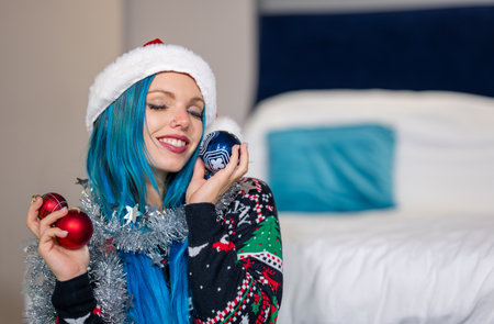 Portrait of a beautiful caucasian hipster woman in Christmas clothes.She keeps her eyes closed while holding colorful balls and a silver decoration around her neck.Beauty,Christmas holidays,positivityの写真素材