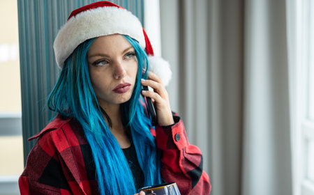A hipster caucasian woman in Christmas clothes. She is talking on her cell phone while looking out the window, she has a cup of tea. Christmas,talking with friends, positivity and happiness.の写真素材