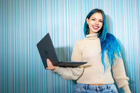 Portrait of beautiful blue haired hipster woman working standing with laptop, looking at camera smiling satisfied and confident. Technology use, problem solving, positivity and success.の写真素材