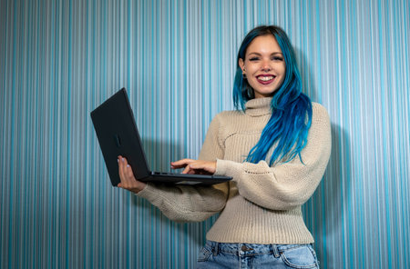 Portrait of beautiful blue haired hipster woman working standing with laptop, typing on keyboard and then turning around looking at camera satisfied and smiling. Problem solving,positivity and successの写真素材
