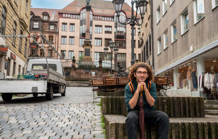 Nuremberg, Germany, August 1, 2023. A glimpse of the old town, with its old houses and street lamps. A young man with curly hair and glasses is sitting on a bench. Travel destinations.の写真素材
