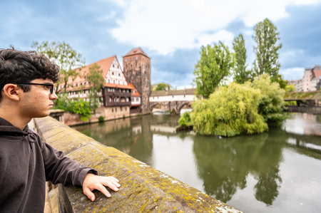 Nuremberg, Germany, August 1, 2023. A young Caucasian man is fascinated by the enchanting view of the river with the half-timbered house reflected in the water. Exploring and discovering Nuremberg.の写真素材
