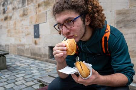 Nuremberg, Germany, August 1, 2023. A young man enjoys a break eating sandwiches with typical Nuremberg sausage. Close up on the sandwich. Relax, lifestyle, local food.の写真素材