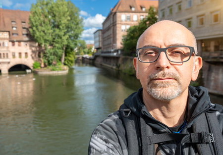Nuremberg, Germany, August 3, 2023. Portrait of a middle-aged man with a view of the Hospital of the Holy Spirit on the Pegnitz River. Cityscape. Travel destinations.の写真素材