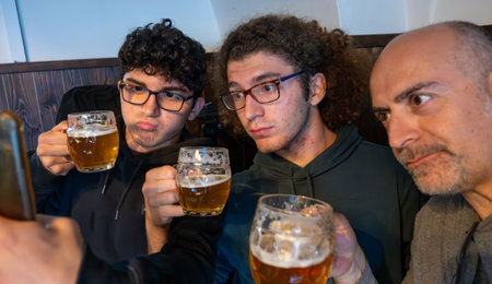 Prague, Czech Republic, August 5, 2023. Group selfie with two young people and a middle-aged man drinking a mug of beer. Lifestyle, drinking together across generations, and the use of technology.の写真素材
