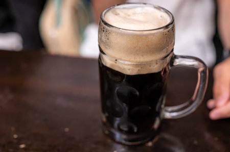 A beautiful, conceptual close-up of a dark beer on the bar counter. The thick head of foam on top...