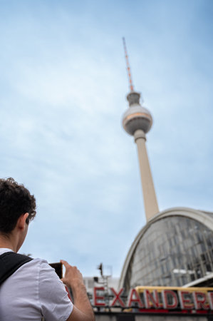 Berlin, germany, august 11, 2023. Person with backpack holding a smartphone, capturing a landmark...