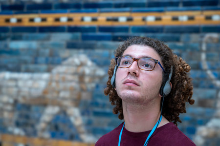 Berlin, germany, august 16, 2023. Young man with headphones and glasses gazes up at the blue-tiled...