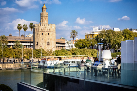 SEVILLE - SPAIN - FEBRUARY 21, 2018: View of the golden tower (Torre del Oro) in Seville, Andalusia, Spain on the Guadalquivir river at sunset, with tourists at the restaurant.のeditorial素材