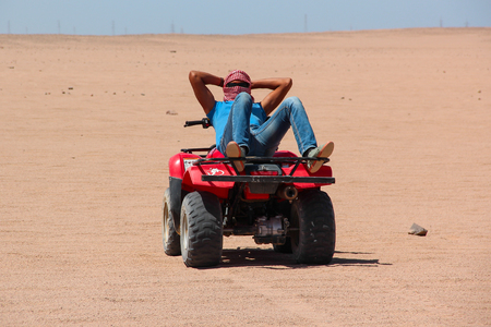 HURGHADA, EGYPT - Apr 24, 2015: An young Egyptian man rests lying on his ATV after desert safari on quad, Egypt, HURGHADA on Apr 24, 2015.のeditorial素材