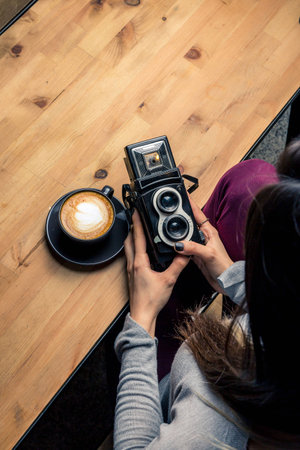 Girl holding an old camera, coffee latte in a dark wooden cupの写真素材