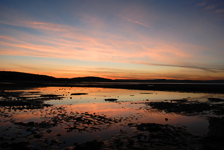 sunrise over the bay with sky reflected in pools in the sandの写真素材