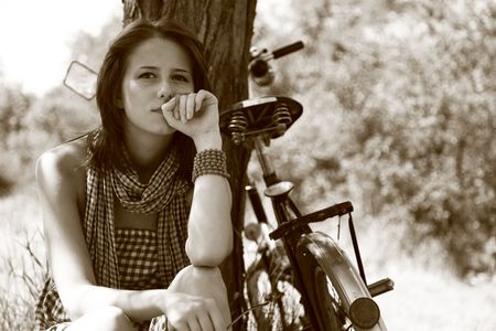 Beautiful girl sitting near bike and tree at rest in forest. Photo in retro style. の写真素材