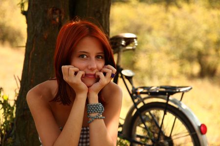 Beautiful girl sitting near bike and tree at rest in forest. 