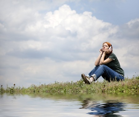 Young smiling girl with headphones sitting at green grasss.の写真素材