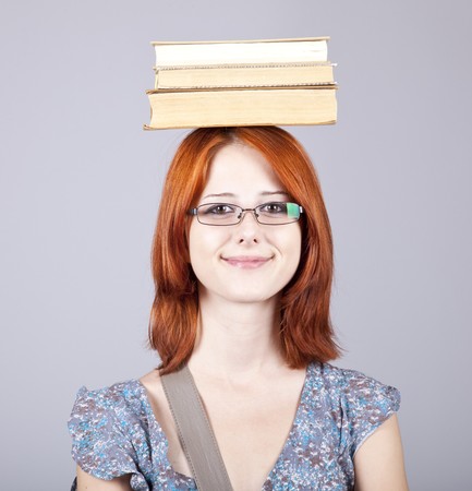 Red-haired girl keep books on her head. Studio shot.の写真素材