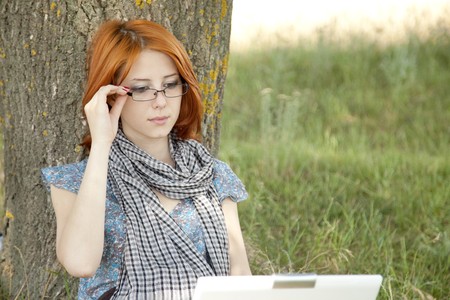 Young smiling fashion girl in glasses and notebook sitting near tree.の写真素材