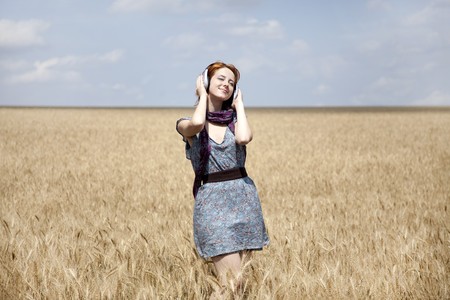 Young  smiling girl with headphones at wheat field.の写真素材