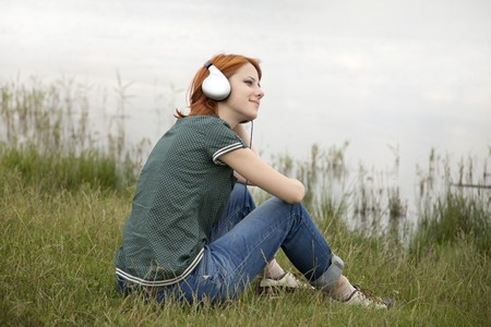 Young fashion girl with headphones sitting at lake coast. の写真素材
