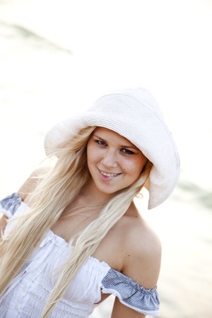 Beautiful young blonde girl in hat on the beach of Black Sea. Sea and sunlight is on background.の写真素材