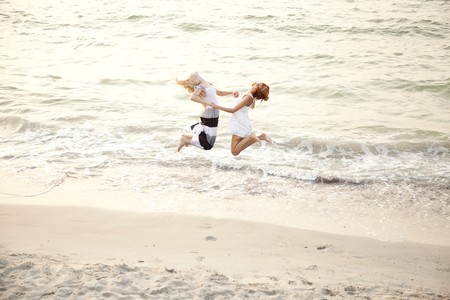 Two beautiful young girlfriends jumping on the beach of Black Sea. Sea and sunlight is on background.の写真素材