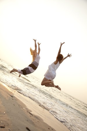 Two beautiful young girlfriends jumping on the beach of Black Sea. Sea and sunlight is on background.の写真素材