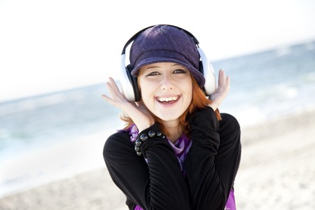 Portrait of red-haired girl in cap with headphone on the beach.