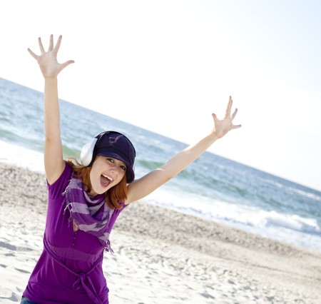 Portrait of red-haired girl in cap with headphone on the beach.
