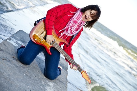 Young brunet girl play on guitar at sea pier in wind day.の写真素材