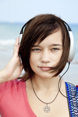 Young brunet girl with headphone and guitar on the beach.の写真素材