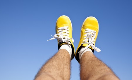 Two foots in yellow sneakers on blue sky background.の写真素材