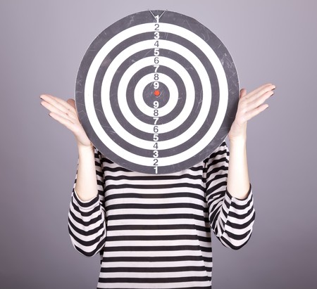 Girl with dartboard in place of head. Studio shot.